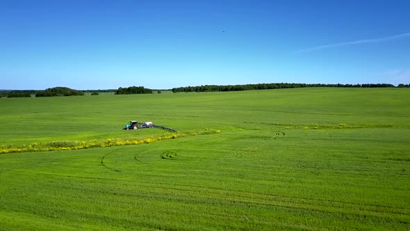 Aerial View Tractor Moves on Green Field Under Blue Sky