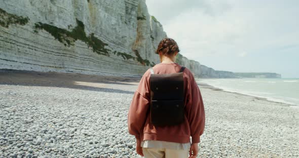 A Young Woman Walks Along a Pebbly Beach Past Sheer Chalk Cliffs