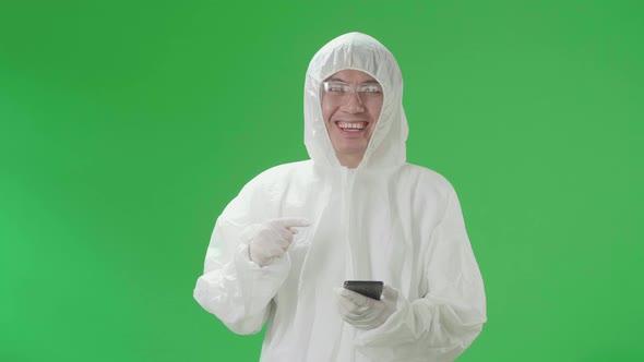 Asian Man Wear Protective Uniform Ppe Use And Pointing To Mobile Phone In The Green Screen Studio