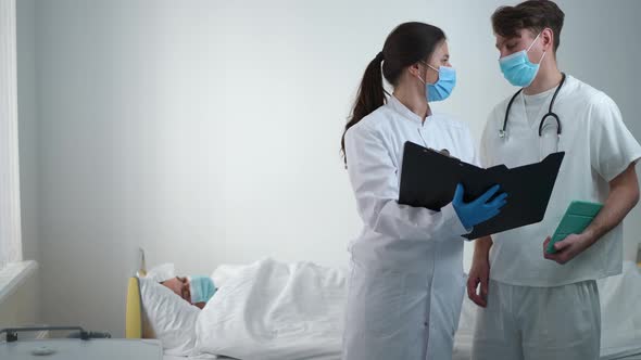 Worried Male and Female Doctors Talking Standing in Hospital Ward on the Right with Blurred Patient