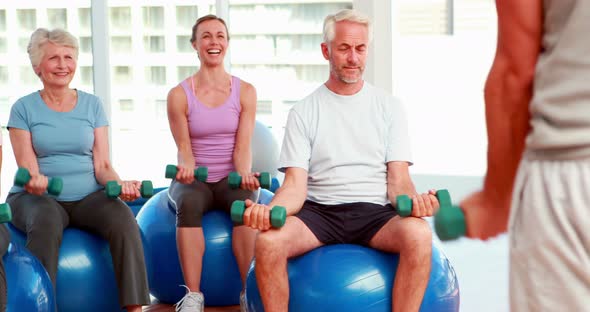 Exercise class sitting on exercise balls lifting hand weights