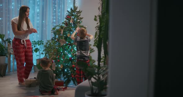 A Family Mother and Two Children Decorate a Christmas Tree with Toys in the Living Room of Their