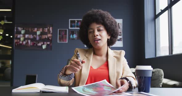 Mixed race businesswoman sitting having a video chat going through paperwork in a modern office