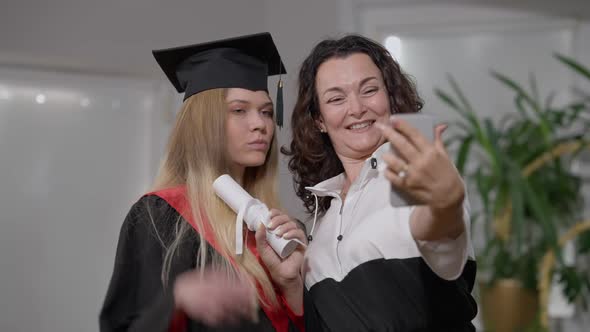 Joyful Happy Mother and Graduate Daughter Taking Selfie on Smartphone Indoors at Home