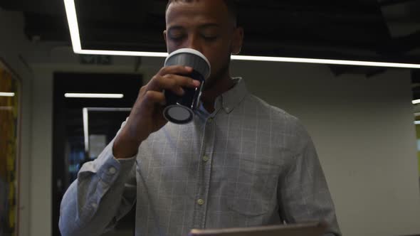 Mixed race businessman walking and drinking a cup of coffee in modern office