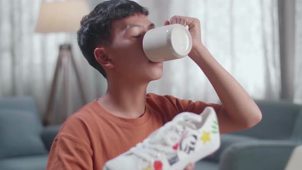 Close Up Of Asian Boy Footwear Designer Drinking Coffee While Working On A Laptop At Home