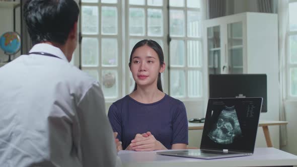 Asian Man Doctor Is Talking With Young Female Patient During Consultation In A Health Clinic