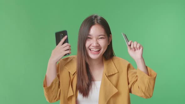 Asian Woman Using Mobile Phone With Credit Card And Celebrating In The Green Screen Studio