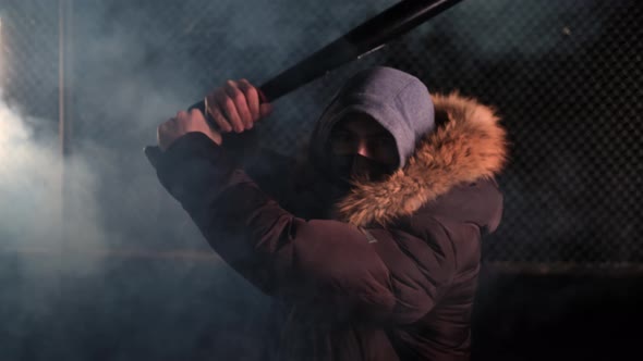 A Masked Man Strikes with a Baseball Bat on a Smoky Street