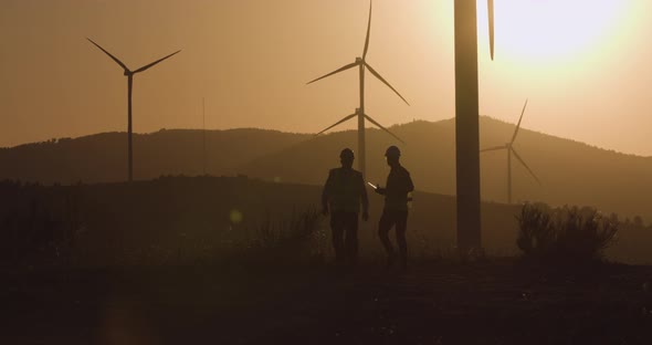 Two Engineers Walk Towards the Camera Turning on the Windmill