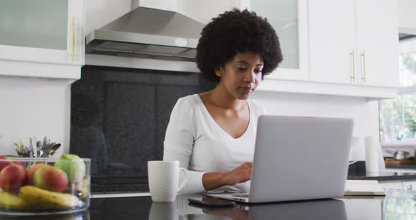 African american woman using laptop in the kitchen while working from home