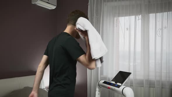 Male fit athlete is walking on running machine and wiping face with towel