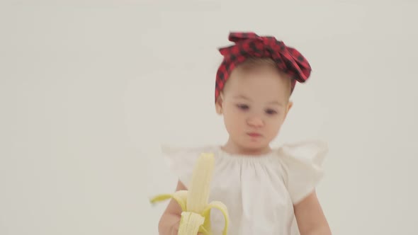 Little girl in plaid headband and skirt is eating big banana