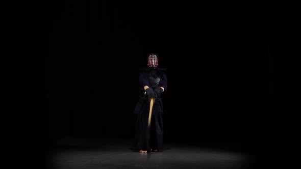 Strong Kendo Guru Practicing Martial Art with the Bamboo Bokken on Black Background.