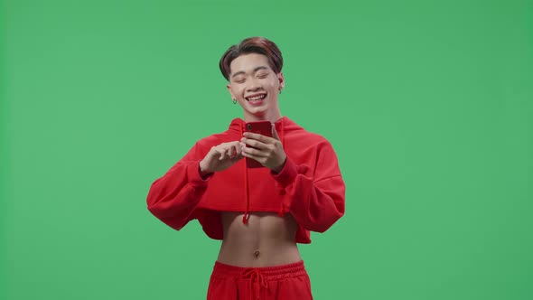 Happy Asian Transgender Male Enjoy Using Mobile Phone While Standing On Green Screen In The Studio