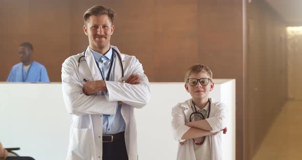 Portrait of Adult and Kid Doctors in Lab Coat Smiling at Camera with Hands Crossed in Hospital