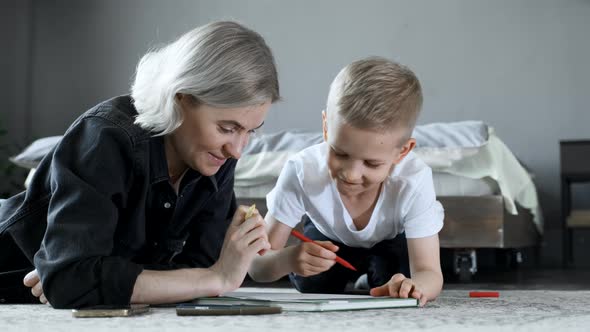 A Young Mother and a Boy Child Are lying on the Floor, Drawing with Felt-Tip Pens on Paper