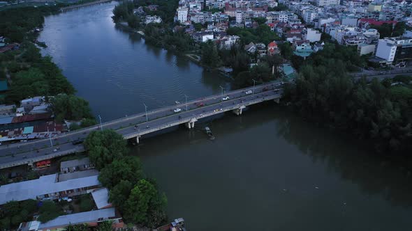 Aerial shot of a river boat going under an urban traffic bridge and waterfront housing along a canal