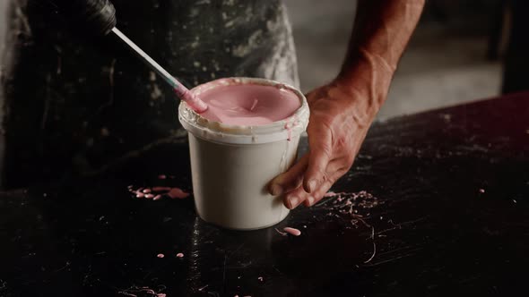 Man works with paint in his trowel. Mixes paint with polymer.