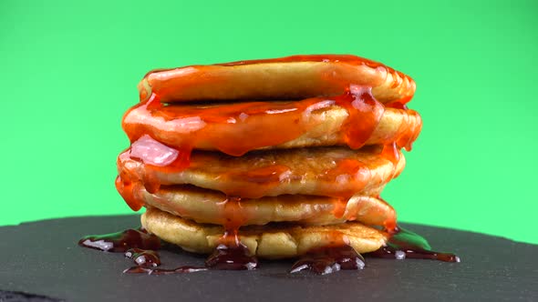 Pancakes with strawberry topping on a green background. Pancake lies on a black slate round stone.