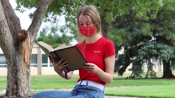 A young student reads while social distancing and wearing a mask on campus.