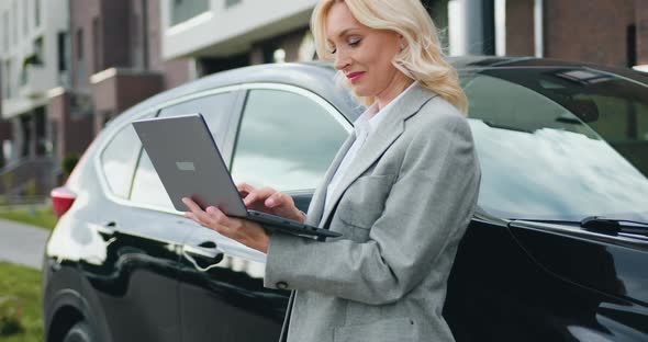 Businesswoman Working on Laptop while their Modern Car in the Background Urban Street