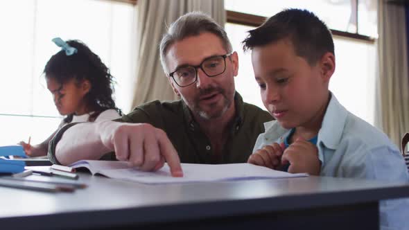 Diverse male teacher helping a schoolboy sitting in classroom reading excersise