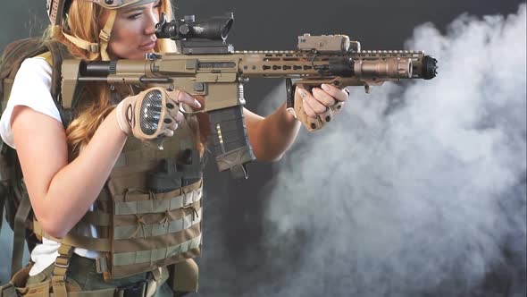 Girl Marksman in Sniper Gear Holding Sniper Rifle in Hand at Dark Smoky Background, Slow Motion