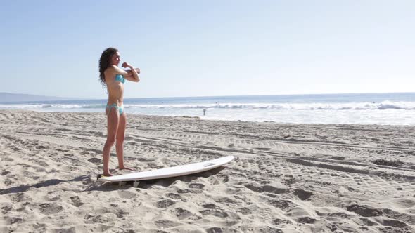 A young woman surfer stretching on the beach.