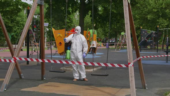 Man wearing protective suit disinfecting the swing with spray chemicals Covid -19. Cleaning concept