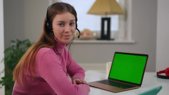 Charming Smart Young Woman in Headphones Posing with Green Screen Laptop in Home Office