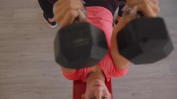 A Focused Young Girl Does a Bench Press with Dumbbells in the Gym and Shakes Her Pectoral Muscles
