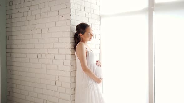 Future Mother Touches Tummy Standing Near Brick Wall in Room