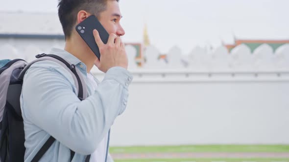 Asian attractive young man backpacker talking on phone walk in city