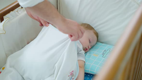 Happy family Caucasian parents take care of sleeping baby boy in bedroom at house in morning.