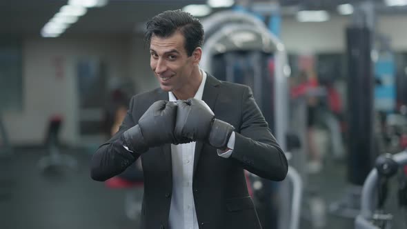 Positive Middle Eastern Man in Suit and Boxing Gloves Looking at Camera Gesturing Smiling