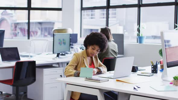 Mixed race businesswoman sitting using a laptop going through paperwork in modern office