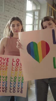 Two Beautiful Young Girls are Standing in the Studio with Lgbt Posters in Their Hands and Looking at