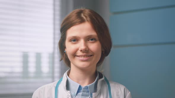 Pretty cheerful young woman general practitioner looks straight and smiles standing