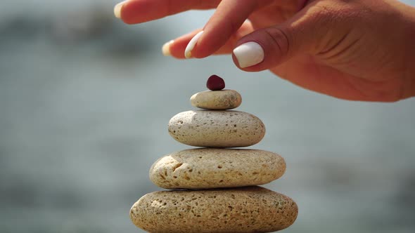 Woman Bilds Stones Pyramid on the Seashore on a Sunny Day on the Blue Sea Background