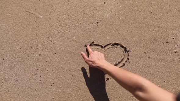 girl draws a heart on the beach. Sea water washes away the drawing on a sandy beach