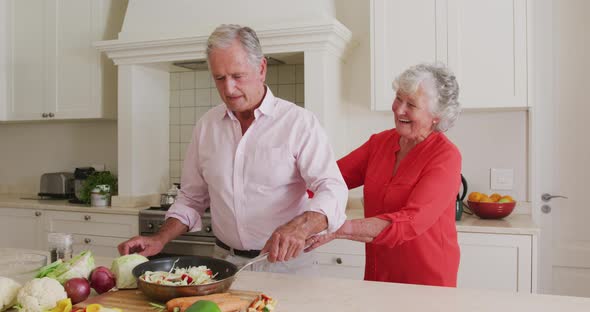 Caucasian senior woman hugging her husband from behind in the kitchen at home
