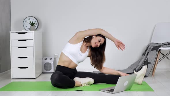 a Young Fit Woman is Watching a Tutorial on Stretching on a Computer