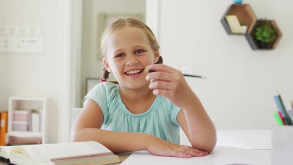 Portrait of caucasian girl holding a pencil smiling looking at the camera at home