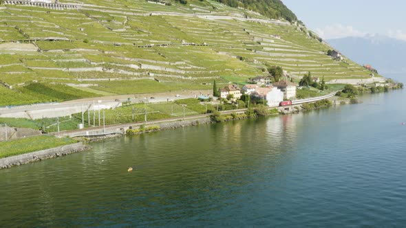 Aerial drone shot going backward over Lake Léman in front of Lavaux terraces. Kayak and swiss train