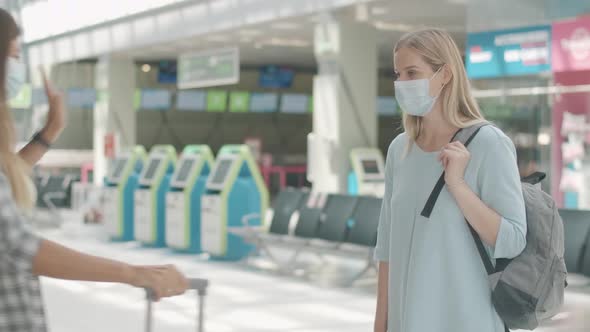 Young Caucasian Women in Face Masks Greeting Each Other in Airport at Arrival Terminal. Conscious