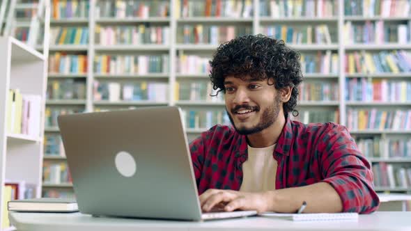 Amazed Happy Excited Stylish Mixed Race Guy Student Sitting in University Library with Laptop