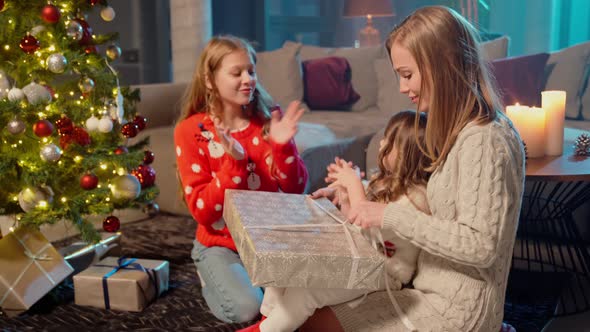 Joyful Sisters Opening Christmas Presents with Their Mother