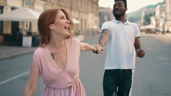 Young Happy Woman Leads Her Boyfriend's Hand Along City Street