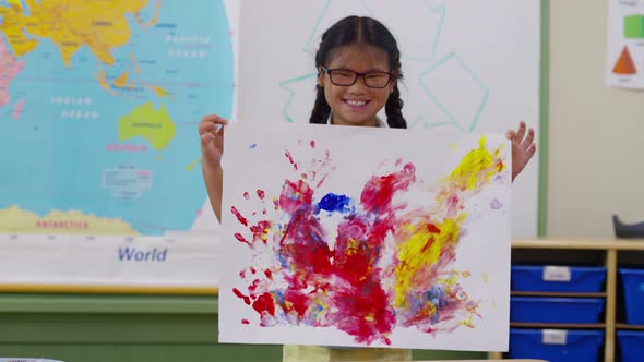 Young girl holds up finger painting project at school